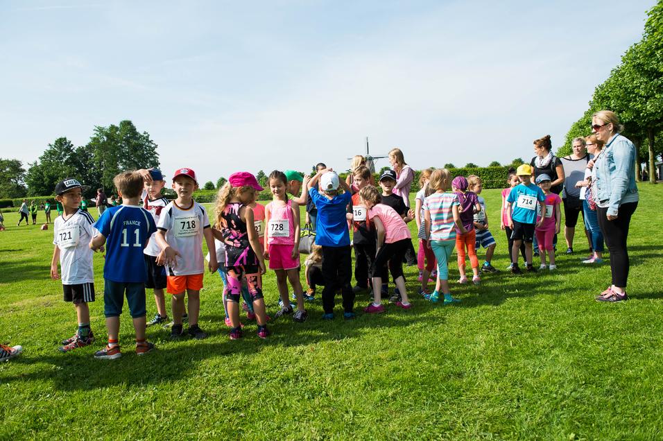 Gruppierung von Kindern in Sportkleidung, die vor einem Laufwettbewerb auf einer grünen Wiese stehen.